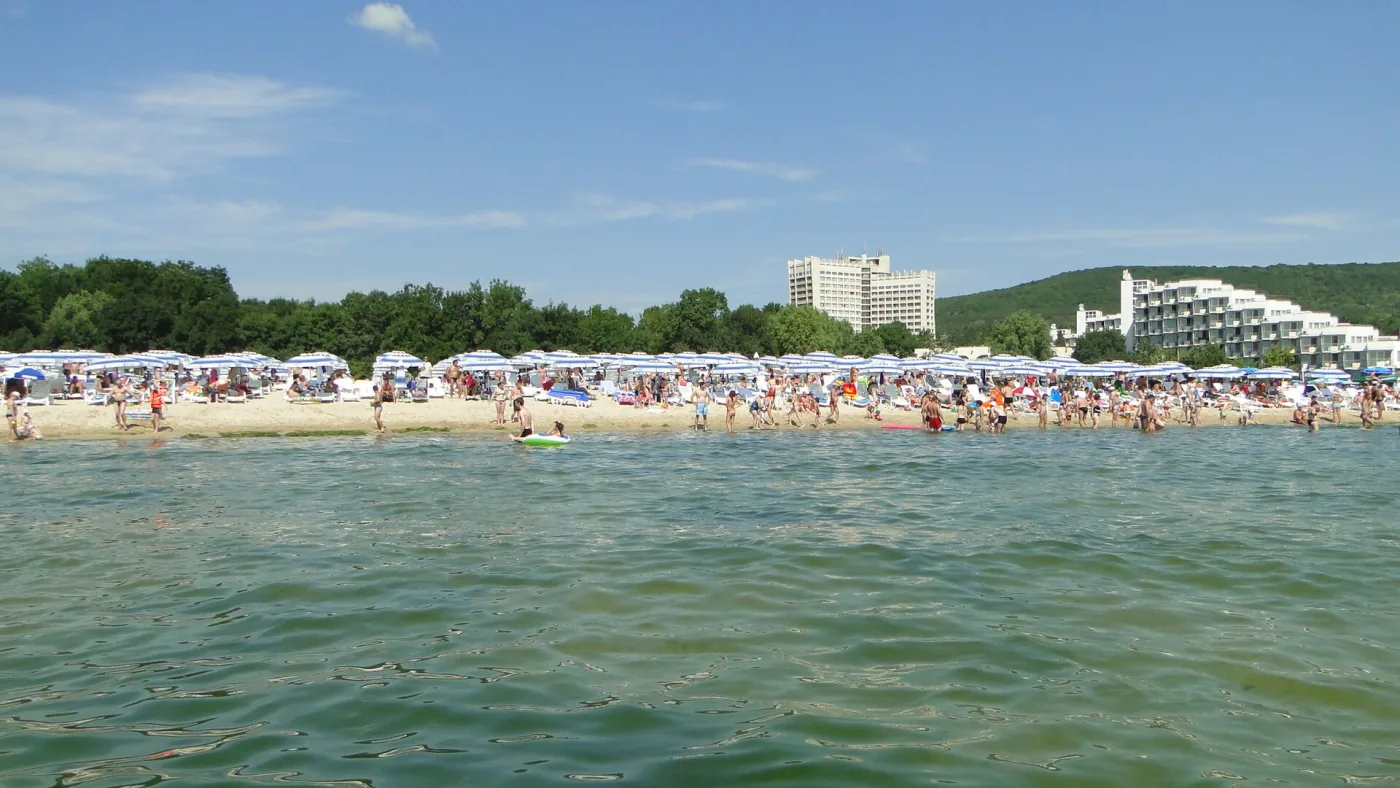 Пляж Албены с воды: ряды зонтов, за ними сосны и корпуса отелей