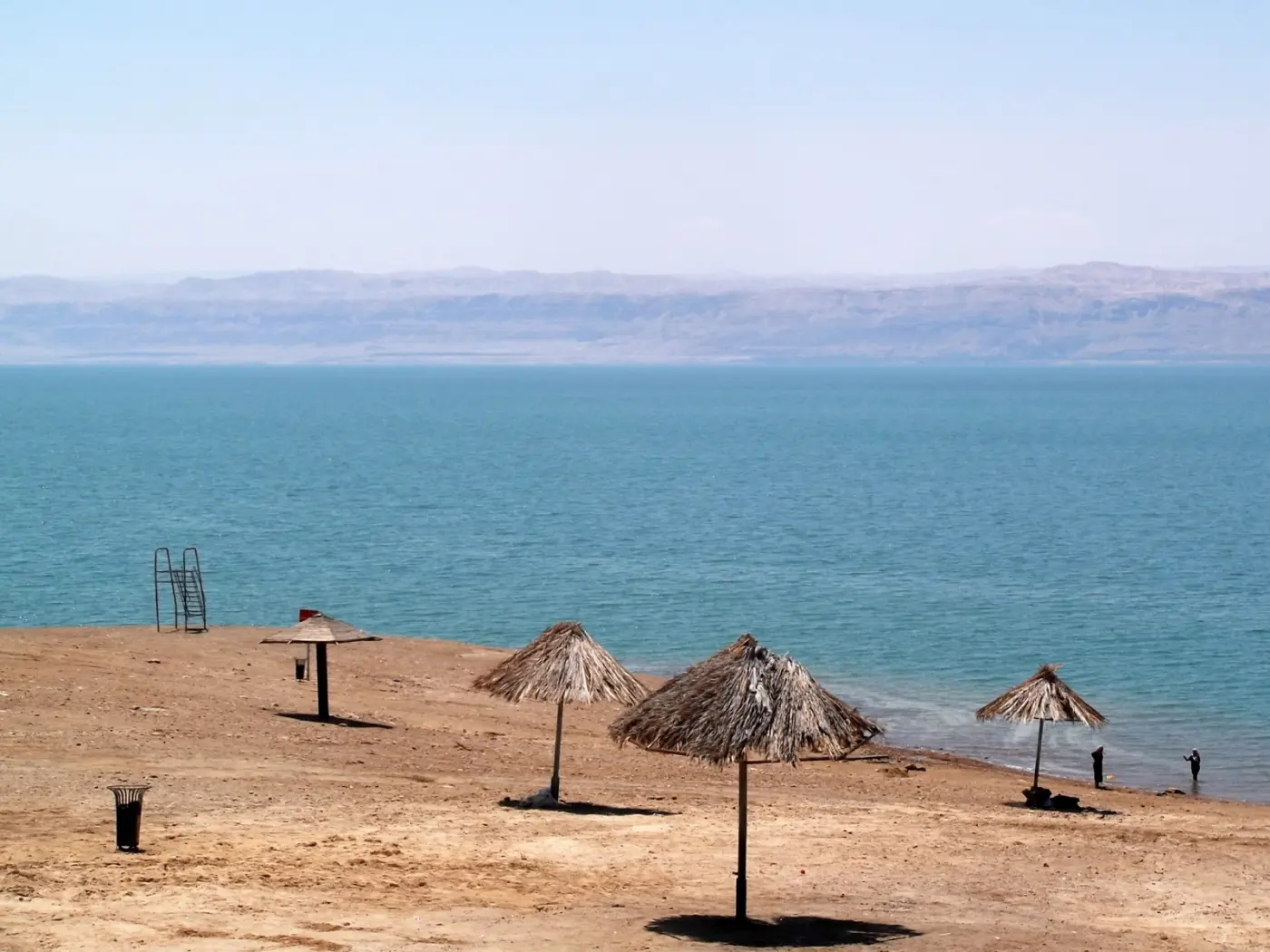 Пляж Мёртвого моря с соломенными зонтами и лестницей к воде